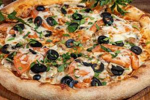 Pizza mit Speck und Käse, Kräutern und Kirschtomaten. mit mozzarella, garnelen und kraken, muscheln und anderen produkten auf holzhintergrund. foto