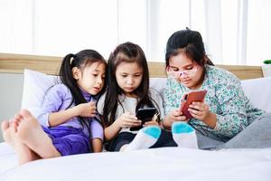 Drei kleine Mädchen spielen zu Hause gemeinsam auf dem Smartphone foto