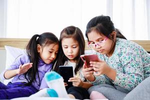Drei kleine Mädchen spielen Smartphone, um zu Hause zusammen zu spielen oder zu lernen foto