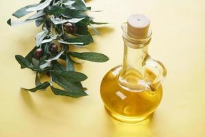 Flasche Olivenöl und frische Oliven in einem Behälter auf dem Tisch.