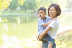 schöne junge asiatische mutter, die kleinen jungen im park trägt, asiatische frau, die glücklich ist, sohn zu haben und kind zu umarmen, mutter liebt und umarmt kind zusammen im sommer, muttertag und familienkonzept. foto