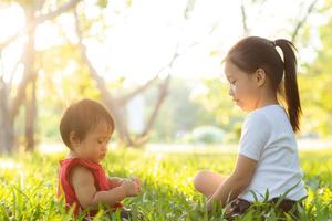 schönes junges asiatisches kind, das im sommer im park spielt, genießt und fröhlich auf grünem gras, kinderaktivitäten mit entspanntheit und glück zusammen auf wiese, familien- und urlaubskonzept. foto