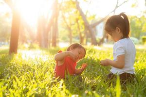 schönes junges asiatisches kind, das im sommer im park spielt, genießt und fröhlich auf grünem gras, kinderaktivitäten mit entspanntheit und glück zusammen auf wiese, familien- und urlaubskonzept. foto