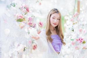 schöne asiatische frau lächelt und steht im weißen rosenblumengarten als natürliches, luxuriöses thema