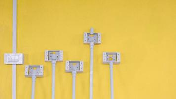Weißer Kunststoff-Lichtschalterkasten mit Rohrleitung und Steckdosen auf gelbem Zementwandhintergrund innerhalb der Hausbaustelle foto