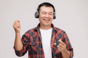 porträt asiatischer mann, der lied oder musik vom schwarzen kopfhörer hört. Studioaufnahme isoliert auf grau foto