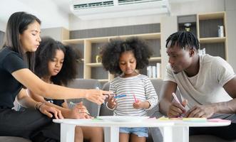 asiatisch-afroamerikanische familie entspannen, plaudern, malen und spaß im urlaub im wohnzimmer des hauses foto