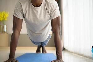 junger afrikaner, der yoga-übungen im wohnzimmer seines hauses macht, mit dem vergnügen, sich bei leichten sportarten in der morgenatmosphäre des tages zu entspannen.