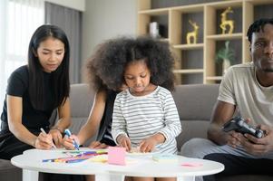 asiatisch-afroamerikanische familie entspannen, plaudern, malen und spaß im urlaub im wohnzimmer des hauses foto