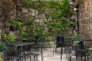 stimmungsvolle Sommerfotografie. Café im Freien mit schwarzen Stühlen und Tischen. Straßencafé im Freien mit vielen Pflanzen foto
