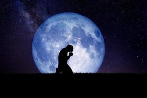 Ein verzweifelter und einsamer Mann kniete nieder und betete zu Gott. Nachts ist im Hintergrund ein Mond. verzweifelte, herzzerreißende und einsame Konzepte foto