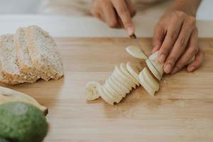 Nahaufnahme von Händen, die Babana schneiden. junge frau, die zu hause gesundes essen kocht. gesundes und wellnesskonzept. foto