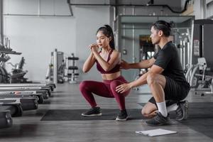 asiatische frau trainiert mit persönlichem trainer im fitnessstudio. asiatische gesunde frau, die mit persönlichem trainer hocken trainiert. foto