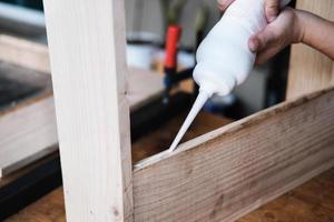 Holzverarbeiter verwenden Klebstoff, um die Holzteile zusammenzusetzen, um einen Holztisch für ihre Kunden zusammenzubauen und zu bauen. foto