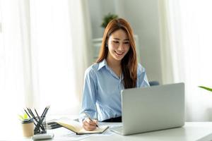 Schönes junges asiatisches Mädchen, das mit einem Laptop in einem Büroraum arbeitet. Konzept des intelligenten weiblichen Geschäfts. foto