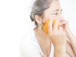 neunundvierzig Jahre alte Frau in einem weißen T-Shirt vor einem weißen Hintergrund mit einer Orange foto