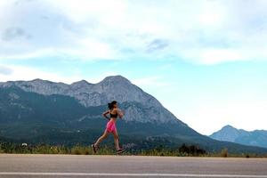 Ein Mädchen läuft auf einer asphaltierten Straße vor dem Hintergrund wunderschöner Berge foto
