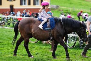 Kleines Mädchen im rosafarbenen Sturzhelm reitet Pony. foto