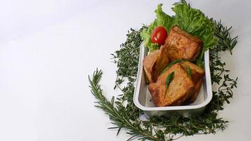 Gebratener Tofu, kleine Tomaten und grüne Chilischoten zusammen mit Salat in einem Aluminiumbehälter, indonesisches Straßenessen auf weißem Hintergrund foto