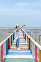 die rückansicht einer asiatischen frau, die auf der regenbogenbrücke steht und fotografiert, um den aussichtspunkt in der provinz samut sakorn zu sehen. foto