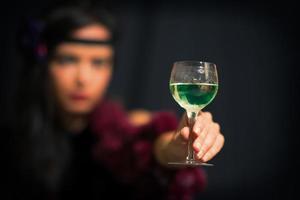 Glas mit Absinth. Er hält eine Hand mit einer verschwommenen Frau foto