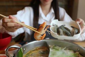 Selektiver Fokus der Frauenhand, die Essstäbchen mit frischen Garnelen mit Gemüse zum Kochen oder Shabu Shabu und Sukiyaki, japanisches Essen, hält foto