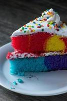 Stück Happy Rainbow Cake mit weißem Zuckerguss und Streuseln foto