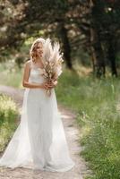 glückliches brautmädchen in einem weißen leichten kleid mit einem strauß getrockneter blumen foto