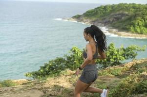 Schöne fitte Frau in Sportbekleidung, die über einen Felsenpfad auf einem Berggipfel am Meer läuft, Gesundheits- und Reisekonzept. foto