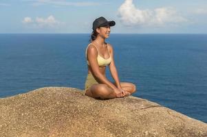 schöne asiatische frau in sportbekleidung, die yoga auf dem berggipfel am meer nach trekking-, reise- und meditationskonzept macht. foto