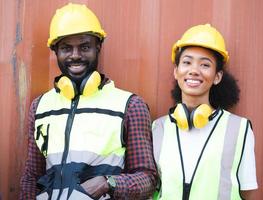 Fröhliches professionelles Ingenieurteam, das im Freien auf dem Containerhof zusammensteht, Porträt. lächelnder afroamerikanischer Vorarbeiter und Afro-Arbeitnehmerin, die eine Pause von ihrer Arbeit am Frachtschifffahrtsterminal machen. foto