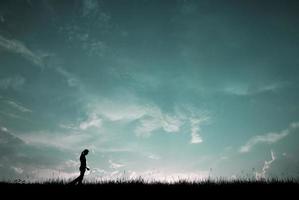 Silhouette einer jungen Frau, die mit blauem Himmel spazieren geht foto