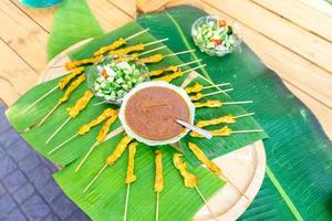 gegrilltes satay-schweinefleisch, thailand traditioneller beliebter lebensmittelstock mit holzstäbchen, fertig gekocht mit einer speziellen sauce daneben. foto