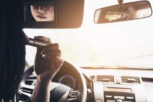 Frau schminkt ihr Gesicht mit Rougepinsel beim Autofahren, unsicheres Verhalten foto