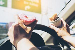 Mann, der Donuts und Kartoffelchips isst, während er Auto fährt - Multitasking-unsicheres Fahrkonzept foto
