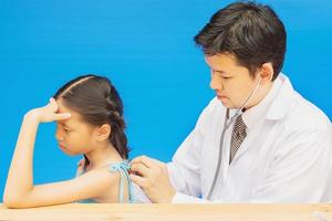 Krankes asiatisches Mädchen wird von einem männlichen Arzt auf blauem Hintergrund behandelt foto