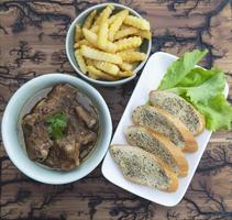 Schweineeintopf mit Pommes frites und Knoblauchbrot servieren foto