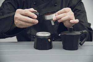 Der asiatische Barista verwendet eine Handkaffeemühle, um heißen Kaffee zuzubereiten foto