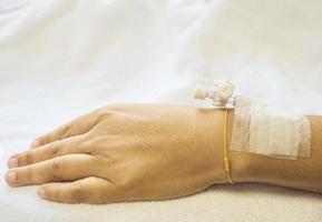 Patientenhand mit Tropfinjektion, Dame auf einem Bett in einem Krankenhaus foto