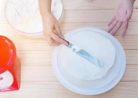 Buttercremekuchen mit Spachtel von Hand aufsetzen foto