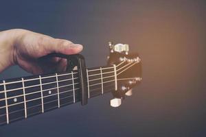 Vintage-Farbbild des Mannes, der Gitarrenkapodaster über grauen Hintergrund legt foto