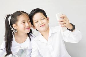 Schöne asiatische Schulkinder machen Selfie, 7 und 10 Jahre alt, auf grauem Hintergrund foto