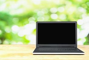 Laptop auf Tischplatte über grünem Baum mit weißem bokeh natürlichem Hintergrund. Foto enthält Beschneidungspfad des leeren Bildschirms.