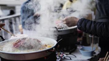 menschen, die gegrilltes schweinefleisch essen, genannt moo kratha, berühmtes essen für kaltes jahreszeitwetter in der bergnatur, moncham, chiang mai thailand - berühmter touristenort foto