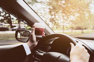 Mann, der Auto fährt, während er eine Tasse Kaffee hält foto