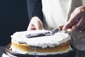 dame, die kuchencreme mit spachtel macht - hausgemachtes bäckereikochkonzept foto