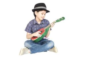 7 Jahre alter asiatischer Junge sitzt und spielt Ukulele isoliert über Weiß. foto