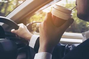 Mann, der Auto fährt, während er eine Tasse Kaffee hält foto