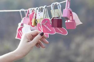 Damenhand, die einen Vorhängeschlossschlüssel mit Herzsymbol der Liebe auf der Brücke hält - Kultur des Liebeszeichensymbolkonzepts foto