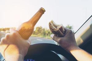 Mann isst Hotdog mit Bier, während er gefährlich Auto fährt foto